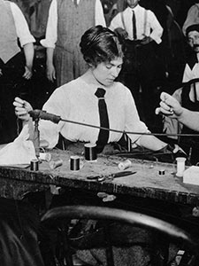 Workers At A Small Bench Hand Finish Garments While Managers Look On